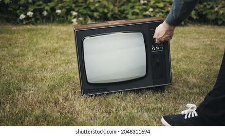 Man Turns On An Old Retro TV Set Standing On The Grass.TV Starts Showing Interference. Concept Of Post Apocalypse, Cyberpunk And Surrealism