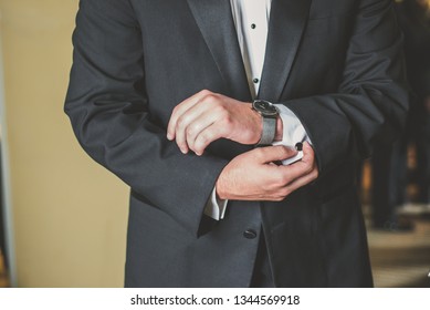 A Man In A Tuxedo Is Buttoning And Fixing His Cuff Links. The Hands Of A Groom In An Elegant Suit Adjusting His Shirt And Watch While Getting Ready.  A Male Getting Dressed For His Wedding Day.