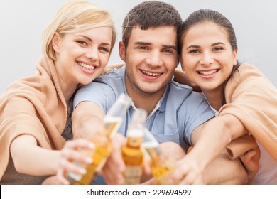 Man and two women relaxing on beach with beer. Happy friends drinking together on beach with focus on friends