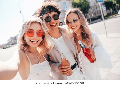 Man and two young beautiful smiling hipster female. Carefree women posing outdoors. Positive models holding and drinking fresh cocktail drink in glass bottle. In the street. Cheerful and happy - Powered by Shutterstock