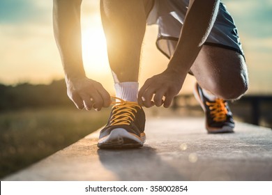 Man tying jogging shoes.A person running outdoors on a sunny day.Focus on a side view of two human hands reaching down to a athletic shoe.