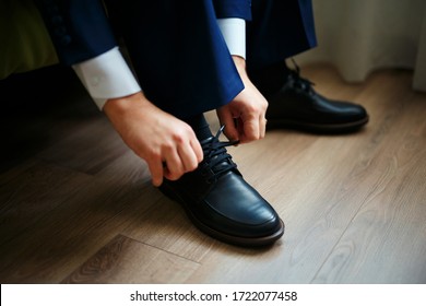 Man Tying The Laces On Black Shoes On A Wooden Floor.