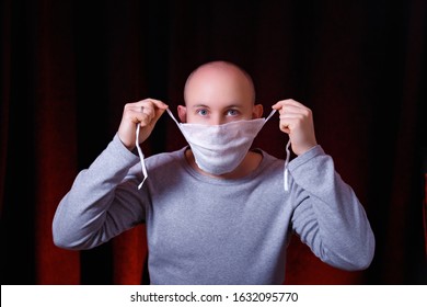 A Man Tying A Medical Gauze Mask On Dark Red Background. Emotion Of Surprise. Virus Preventive Methods. Protection Of Upper And Lower Respiratory System From  Chinese Coronavirus Concept.