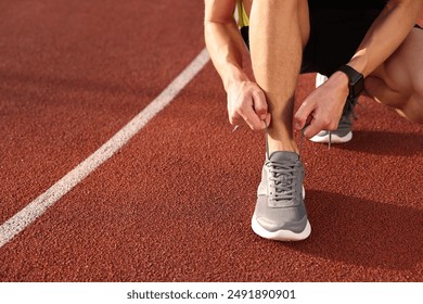 Man tying shoelace of grey sneaker at stadium, closeup. Space for text - Powered by Shutterstock