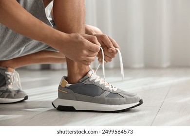 Man tying shoelace of sneaker indoors, closeup - Powered by Shutterstock