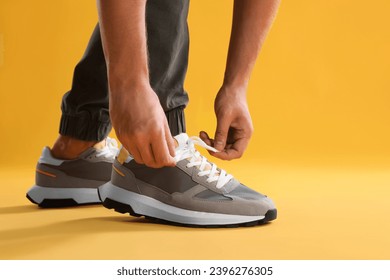 Man tying shoelace of sneaker on yellow background, closeup - Powered by Shutterstock