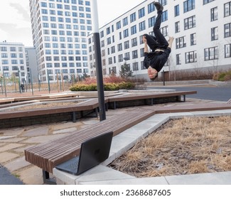 A man types on a laptop outdoors and then does a somersault.  - Shutterstock ID 2368687605