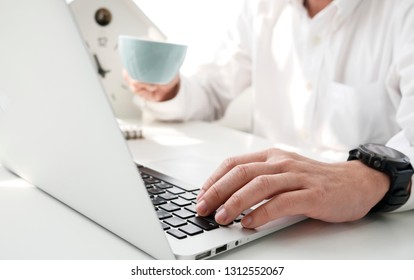 man typing with laptop while work with cup of coffee on foreground on white surface