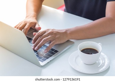 A man typing on laptop computer with a cup of black coffee beside