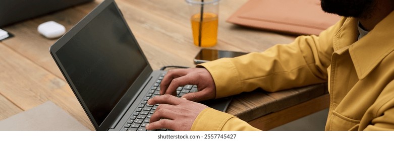 Man Typing on Laptop at Wooden Desk with Orange Juice - Powered by Shutterstock