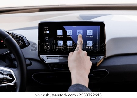Man typing touchscreen inside his auto. Man sitting in front of the handlebar of his own luxury auto. Male finger using an intelligent multimedia touchscreen system for modern electric automobiles.