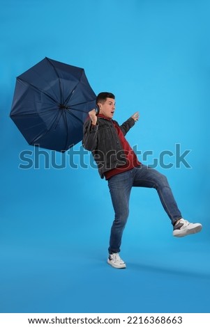 Man with umbrella caught in gust of wind on light blue background