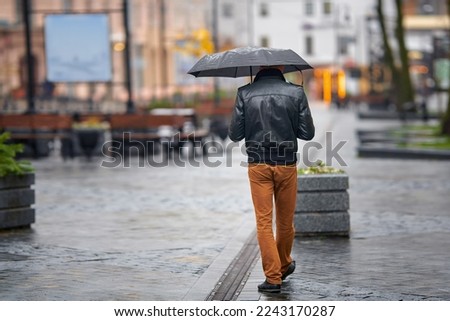 Man with umbrella walk on city street on rainy day. Alone man with umbrella. Back view of stylish man in rainy weather