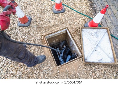 Man Unblocking Domestic Sewage Drain Through Open Inspection Chamber, Drain Cleaning Company, UK