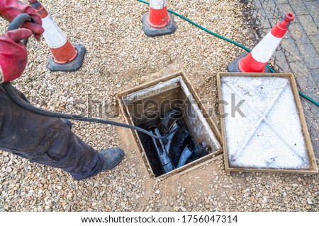 Man unblocking domestic sewage drain through open inspection chamber, drain cleaning company, UK