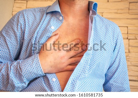 Man unbuttoned his shirt on his chest and placed his hand on sternum area because of severe pain behind his sternum or chest. Concept photo of symptom of heart pain, heartburn, myocardial infarction