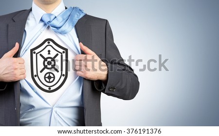 A man in an unbuttoned shirt with an image of shield resembling a safe door on his chest. Front view. Grey background. Concept of security.