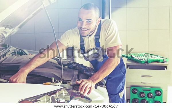 A man\
in uniform in a car repair shop repairs the\
car