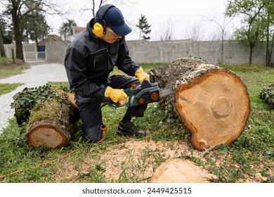 A man in uniform cuts an old tree in the yard with an electric saw.