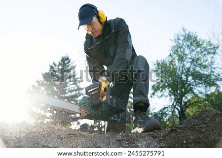 A man in uniform cuts an old tree in the yard with an electric saw