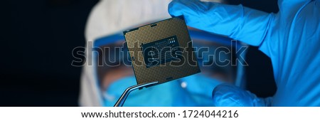 Man in uniform holds microprocessor with forceps. Software-controlled device for processing information. Repair microprocessor electronics electrical equipment. Engaged in chip implementation