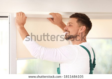 Man in uniform installing roller window blind indoors