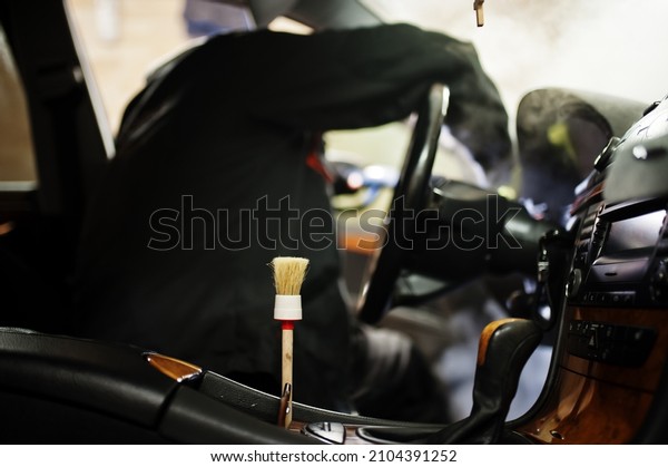 Man in\
uniform and respirator, worker of car wash center, cleaning car\
interior cleaning brush . Car detailing\
concept.