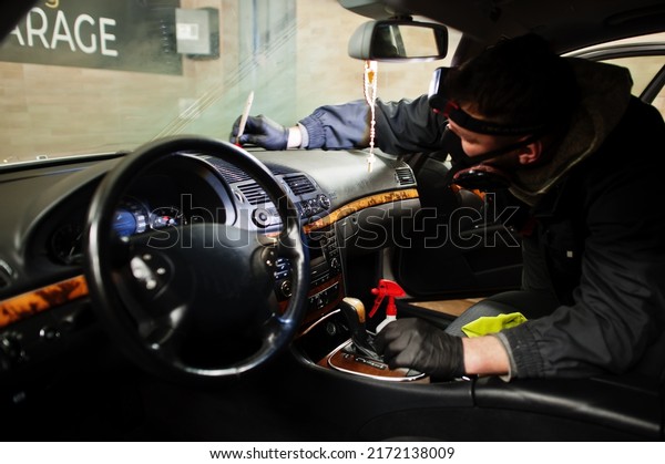 Man in\
uniform and respirator, worker of car wash center, cleaning car\
interior cleaning brush . Car detailing\
concept.