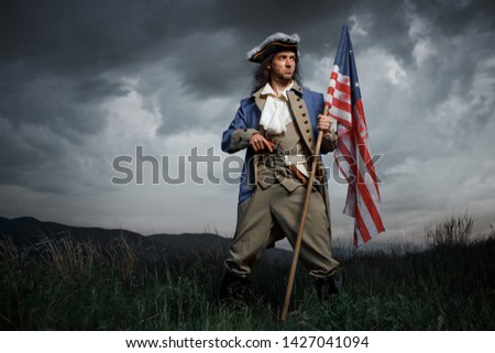 Man in United States War of Independence soldier costume with flag posing in forest. 4 july independence day of USA concept photo composition