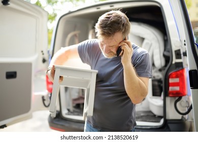 Man Unloading Pickup Truck And Bringing Furniture To New House On Moving Day. Person Is Talking On The Phone. Rental Of Car For Moving.