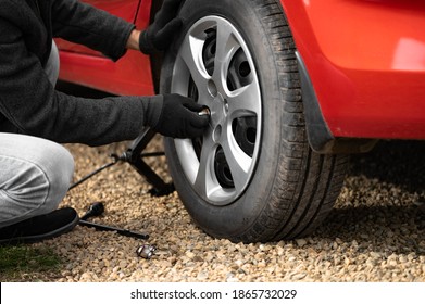 A man unscrews or screws the rear wheel of a red car with summer tires. The concept of puncturing a tire or replacing a winter wheel with a summer one with your own hands
