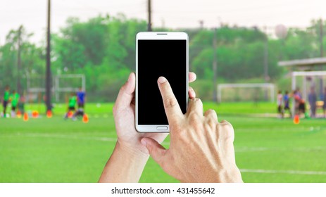 Man Use Mobile Phone, Blur Image Of Children Are Playing Football As Background.