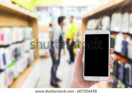 Man use mobile phone, blur image of inside cell phone accessories shop as background.