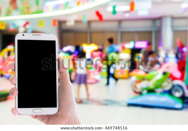 Man use mobile phone, blur image of game zone\
in the mall as background.