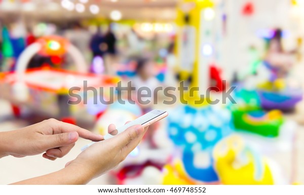 Man use mobile phone, blur image of game zone\
in the mall as background.