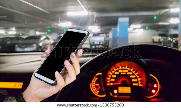 Man use mobile phone in the car, blur\
image of parking in the building as\
background.
