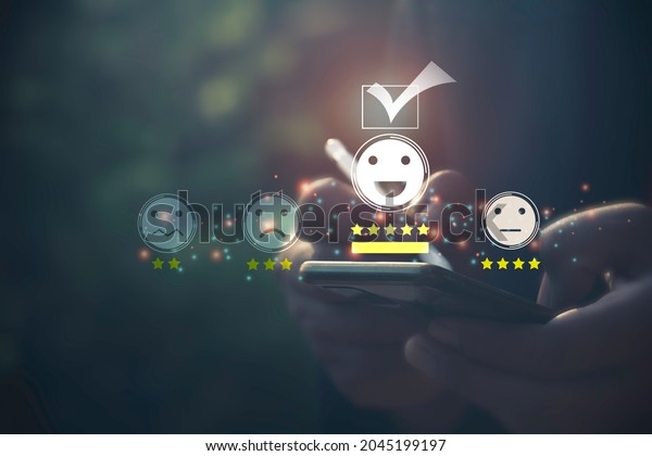 A man use mobile phone check mark face emoticon\
smile on dark background.Customer service,service mind,service\
rating.Photo concept of satisfaction survey and smiling face icons\
time.