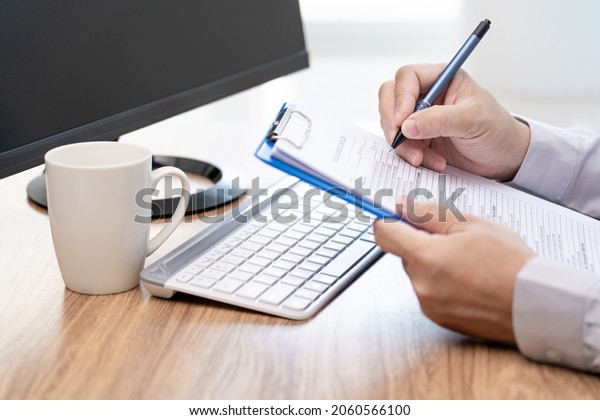 A man\
use pen write on document about car repairs and use desktop\
computer working and coffee cup on table in\
office