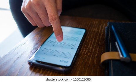 A man use smart phone show calendar year 2019 app on screen, scheduling and booking appointment or meeting and working, a blue pen and black diary notebook on the wooden table, business concept