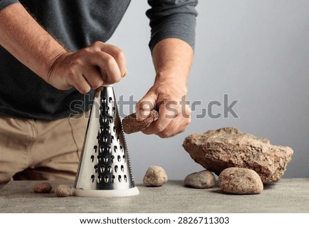 Man uselessly grating a stone on a kitchen grater, illustrating pointless work, wasted effort and inefficient processes. Conceptual image about bureaucracy, meaningless tasks, unnecessary labor and working hard without achieving a useful result.