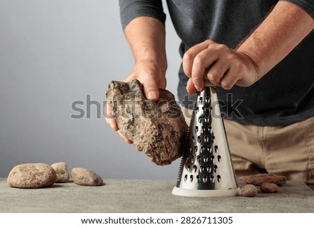 Man uselessly grating a stone on a kitchen grater, illustrating pointless work, wasted effort and inefficient processes. Conceptual image about bureaucracy, meaningless tasks, unnecessary labor and working hard without achieving a useful result.