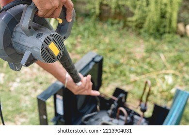 A Man Uses An Electric Air Blower To Dry A Cleaned And Washed Window Type Air Conditioning Unit Outside. Aircon Cleaning Service.