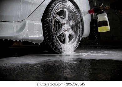 A Man Uses A Hand Pump Car Foam Sprayer On The Rims Of A Car. At A Carwash Or Auto Detailing Shop. Flash Illuminated.