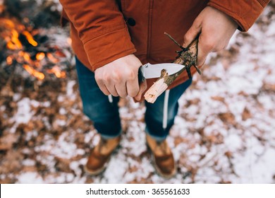 A man uses a knife to whittle a stick out hiking