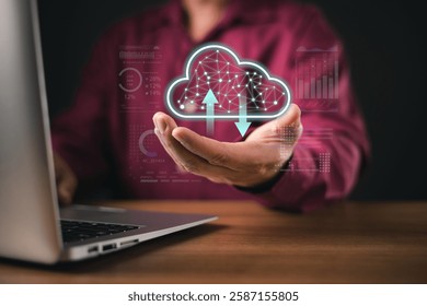 A man uses a laptop while holding a futuristic holographic cloud icon with upload and download symbols. The digital interface represents cloud computing, data storage, and tech innovation.