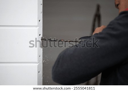 A man uses a large drill to make a hole for a lock in a very close door.