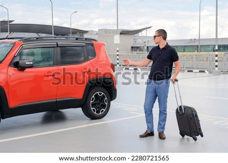 A man uses a remote control to lock or unlock a car in a parking lot. Security system and remote central locking concept