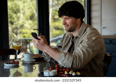 Man uses a smartphone to work in the kitchen in the morning. - Shutterstock ID 2331107345