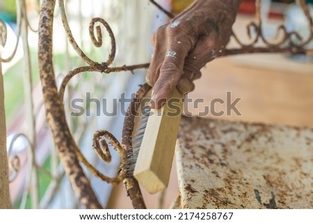 A man uses a steel brush to scrape off old paint and rust from an old wrought iron chair. Furniture repair and restoration concept.