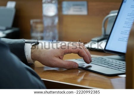 Man uses the touchpad of a small thin laptop while sitting at a wooden table in the office. Official, accountant, businessman or lawyer. No face. Selective focus. Close-up 